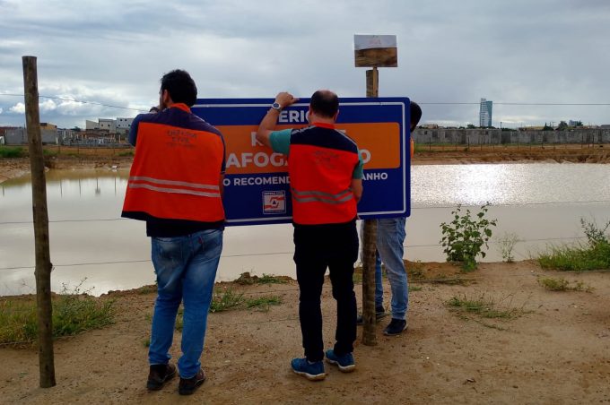 Placas da Defesa Civil alertam para risco de afogamento no entorno da bacia de contenção do Vila América